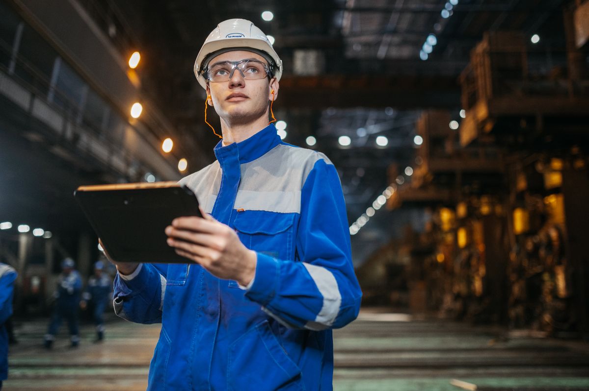 Engineer in safety gear inspecting a factory floor with a tablet