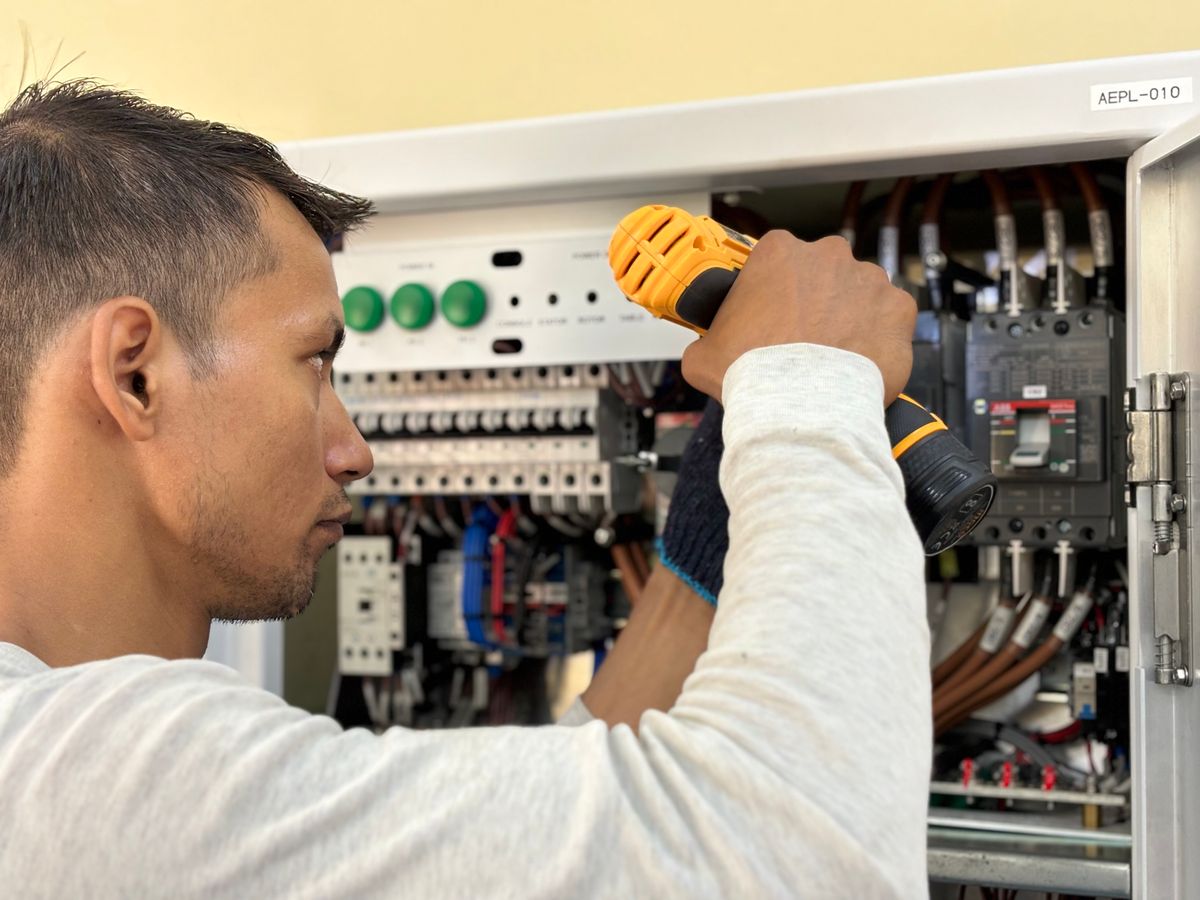 Electrician servicing an opened motor control panel with a cordless drill