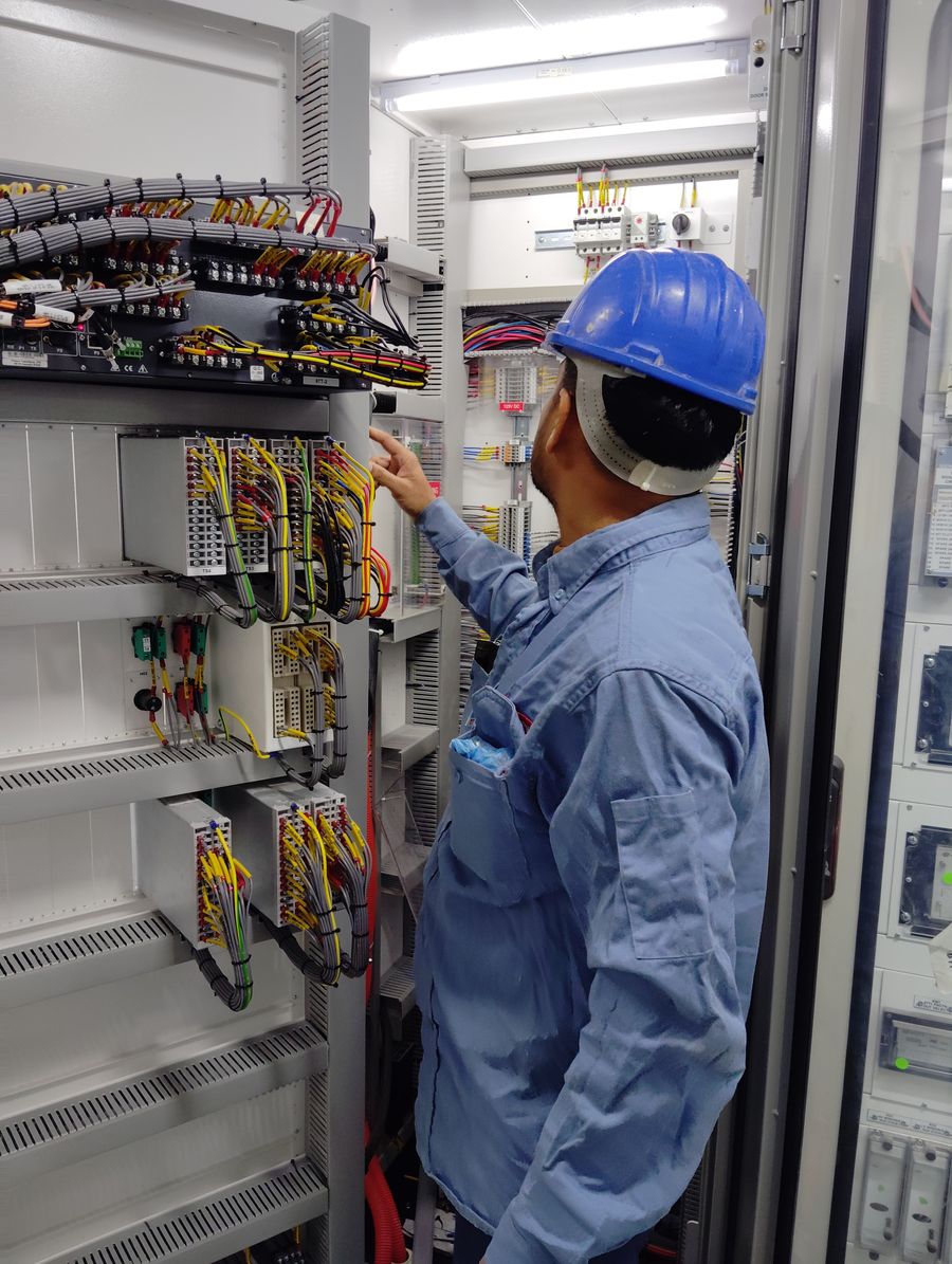 Technician in a hard hat working inside a wired automation cabinet